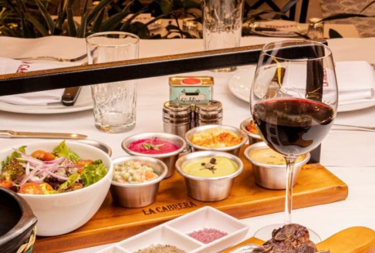 A spread of assorted dips and a salad sit on a restaurant table with a glass of red wine.
