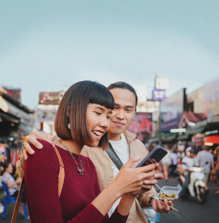 Two travelers leave a review on a smartphone in the center of a busy marketplace.